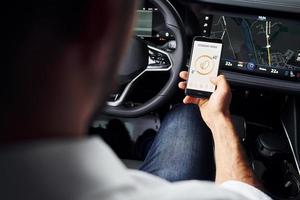 Sits in the car. Close up view of man's hand that holds phone with labels and icons. Conception of remote control photo