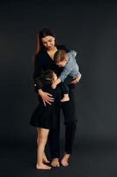 Woman in black stylish clothes is with her little son and daughter in the studio photo