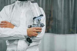 In protective white uniform. Man is working in the auto service photo