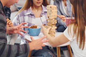 Playing wooden tower game. Group of friends have party indoors together photo