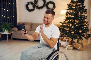 Using smartphone to communicate with people. New year is coming. Disabled man in wheelchair is at home photo