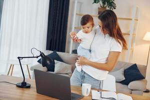 Laptop is on the table. Mother with her little daughter is at home together photo