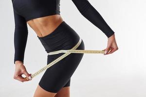 Close up view of sportive woman with measuring tape in the studio against white background photo