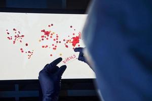 la mano del hombre sostiene una lente con el título del virus contra el fondo con un mapa mundial de infección foto