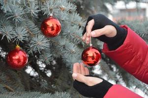 The girl holds a red ball in her hand and hangs it on the Christmas tree. Christmas decorations. Holiday. photo