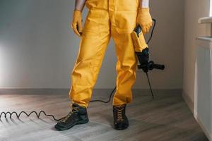 Handyman in yellow uniform with drill standing indoors. House renovation conception photo