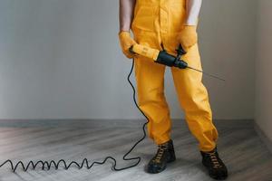 Handyman in yellow uniform with drill standing indoors. House renovation conception photo