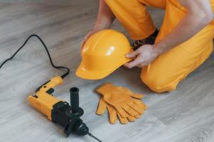 Handyman in yellow uniform with drill standing indoors. House renovation conception photo