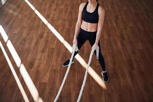 On the floor illuminated by light beams. Young sporty woman in sportswear doing fitness by using knots photo