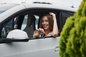 Feeling happy. Female driver showing her keys while sits inside of automobile photo