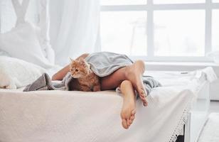 Legs of the sleeping girl on the white bed. Cute cat is awake and wants to go somewhere photo