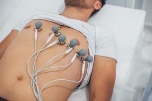 Man lying on the bed in the clinic and getting electrocardiogram test photo