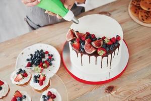 Close up view of woman pouring cream on the pie in the kitchen photo