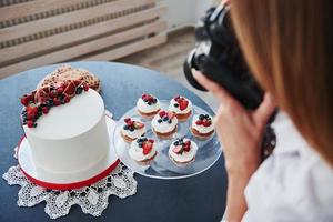 Woman stands in the kitchen and takes photo of her homemade cookies and pie by using camera