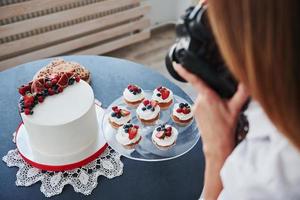 Woman stands in the kitchen and takes photo of her homemade cookies and pie by using camera