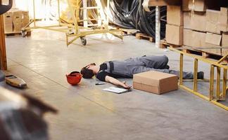 Warehouse worker after an accident in the storage. Man in uniform lying down on the ground photo