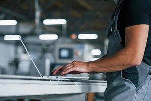 Modern laptop. Typing on keyboard. Industrial worker indoors in factory. Young technician with orange hard hat photo