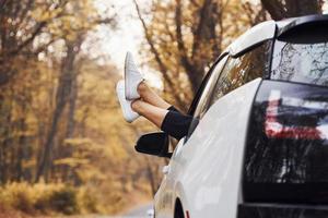 Woman's legs is off the car window. Modern brand new automobile in the forest photo