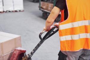 Young male worker in uniform is in the warehouse pushing pallet truck photo