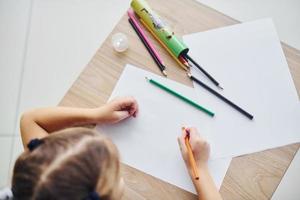 vista superior de la niña con lápices y hoja de papel vacía sobre la mesa foto