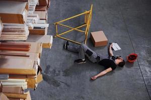 Warehouse worker after an accident in the storage. Man in uniform lying down on the ground photo