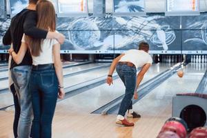 Rolling ball. Young cheerful friends have fun in bowling club at their weekends photo