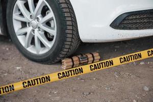 explosivo peligroso cerca de la rueda del coche blanco moderno. cinta amarilla de precaución en el frente foto