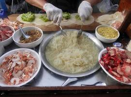 Seller hands in gloves preparing fresh spring roll filling with Red pork, shrimp, bean sprout and radish for take away to customer. Applied menu served on the Thai street food market. photo