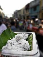 Local Thai dessert in plastic box, mixed of Thai sweet meat and shredded young coconut on banana leaf, morsels, White fuzz coconut, fluffy, blurred background of Thai street food market photo