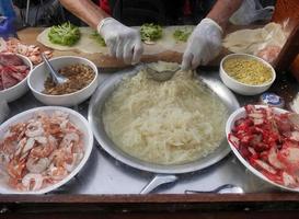 Seller hands in gloves preparing fresh spring roll filling with Red pork, shrimp, bean sprout and radish for take away to customer. Applied menu served on the Thai street food market. photo