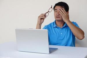 Asian man, feels hurt his eyes, holds eyeglasses during working on laptop. concept , Eyesight problem. Optometry. Glasses with convex or concave lenses. Myopia.Eye disease photo