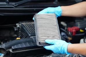 las manos del mecánico de primer plano sostienen la almohadilla del filtro de aire del motor del coche para comprobarlo. concepto, coche roto, servicio de reparación y mantenimiento. El filtro de aire sucio debe cambiarse por uno higiénico. foto