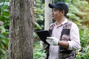 Encuesta botánica masculina asiática y recopila información de plantas botánicas mediante el uso de tabletas inteligentes. concepto, utilizando tecnología de dispositivos inteligentes para gestionar el entorno y los árboles de investigación. foto