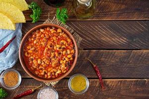 Chili con carne in a bowl on wooden background. Mexican cuisine. Top view photo