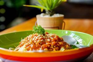 Spaghetti with minced pork and tomato sauce look tasty on colorful ceramic plate, green plant decoration and wooden table in the restaurant. photo