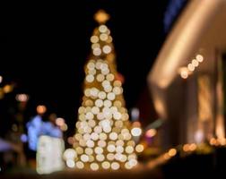 vista borrosa y bokeh del árbol de navidad y decorar la iluminación led frente al centro comercial en la noche de navidad en la ciudad urbana. foto