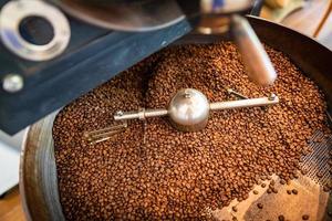 granos de café aromáticos recién tostados en una moderna máquina tostadora de café. tostador de café, fondo de granos de café foto