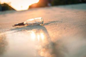 mensaje en la botella arrastrada a tierra contra la puesta del sol. botella con un mensaje foto