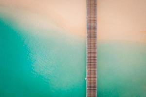 White sand beach wooden pier with transparent blue and turquoise water, aerial top down view from drone on tropical island in Maldives. Beautiful vacation travel destination. photo