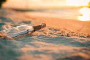 Message in the bottle washed ashore against the Sun setting down romantic shore, soft sand sun rays photo