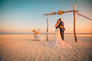 The bride and groom under archway on beach. Romantic wedding background. Bride and groom romantic newlyweds, honeymoon on the beach sunset concept photo