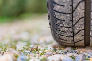 primer plano de la banda de rodadura de los neumáticos de coche en el camino de entrada en un brillante día de verano, guijarros y flores diminutas con hierba foto