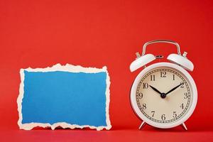 Classic alarm clock with bells and empty torn paper sheet on the red background. photo