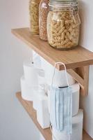 existencias de rollos de papel higiénico, máscara protectora y productos en el estante en casa foto