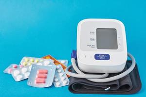 Digital blood pressure monitor and medical pills on a blue background photo