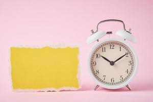 despertador blanco y hoja de papel rota vacía sobre un fondo rosa. concepto de tiempo foto