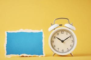 Classic alarm clock with bells and empty torn paper sheet on yellow background photo