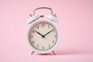 White retro alarm clock on the pink background with copy space. Time concept photo