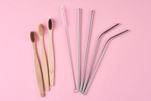 Reusable stainless steel straws and bamboo toothbrushes on pink background