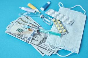 pastillas, máscara protectora, artículos médicos y billetes de dólar en el fondo azul